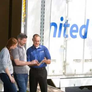 A couple in front of a United moving truck reviewing paperwork with a driver.