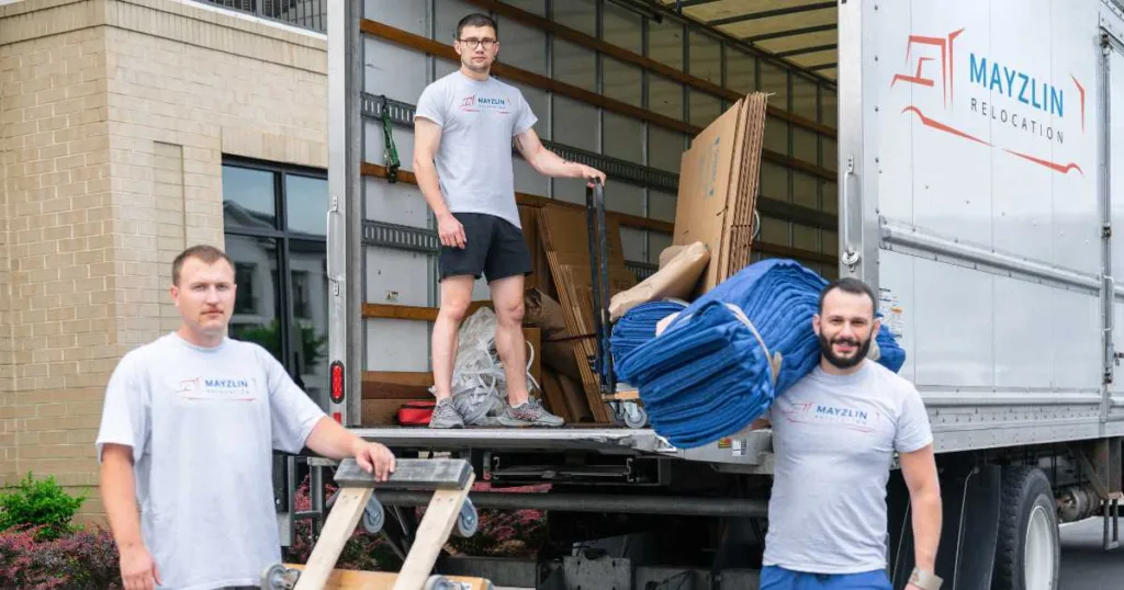 Three Mayzlin movers in the back of a truck with dollies and blankets.