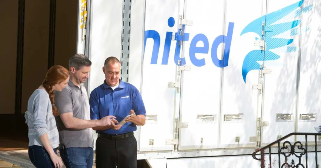 A couple standing in front of a United moving truck, reviewing paperwork with the driver.