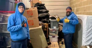 Two movers posing in front of the contents of a storage unit.